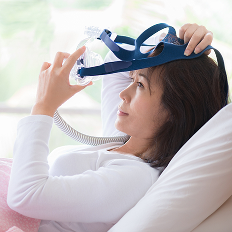 Woman in bed placing a C PAP mask over her face