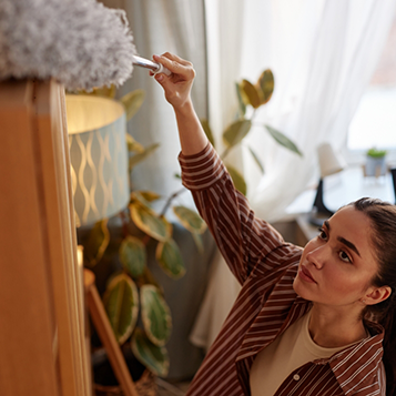 Woman dusting a high bookshelf