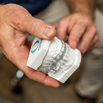 Hands holding a model of the teeth with a clear oral appliance over each arch